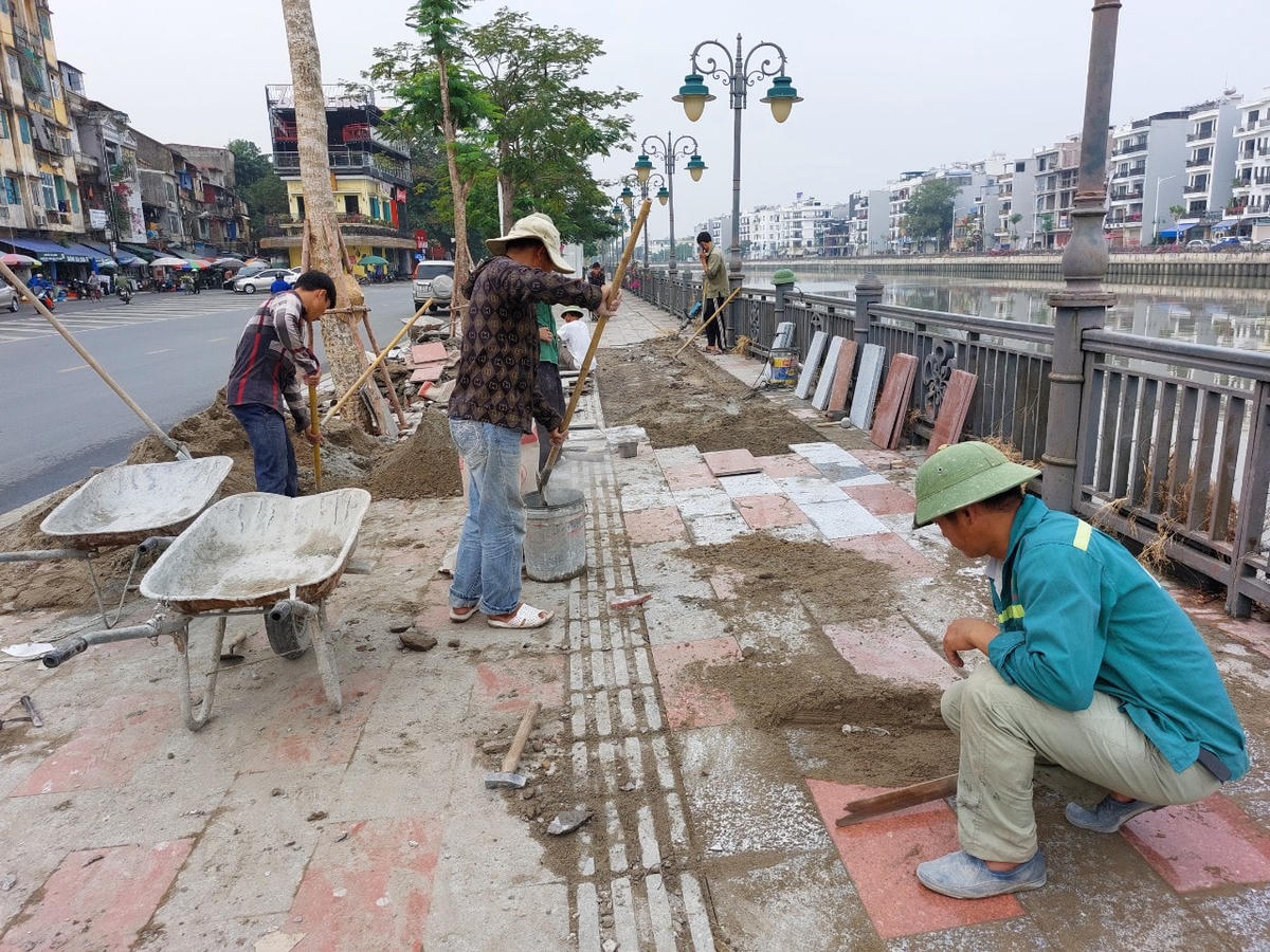 Công nhân đang thay lại lớp đá bị bong, vênh giữa phần lát vỉa hè với tường bao kè bờ sông.