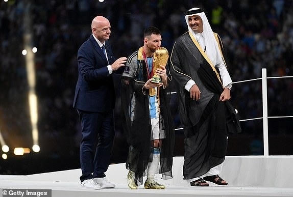 Ngôi sao người Argentina vinh dự được Quốc vương Qatar trao tặng áo choàng truyền thống đồng thời nhận Cúp vô địch từ tay chủ tịch FIFA trong lễ vinh danh sau trận chung kết (Ảnh: Getty).