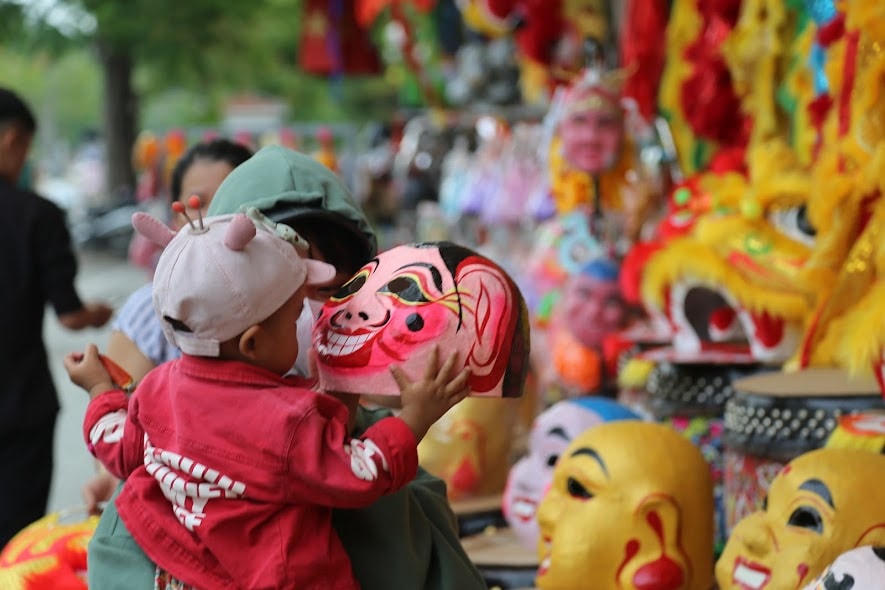 Một em nhỏ thích thú với chiếc mặt nạ ông địa tại một cửa hàng nằm trên đường Trần Hưng Đạo, thành phố Huế.