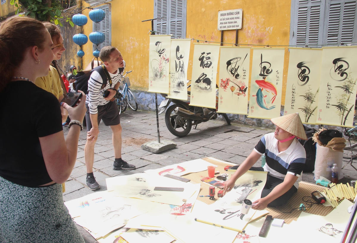Du khách nước ngoài ngồi xem ông đồ vẽ và cho chữ.