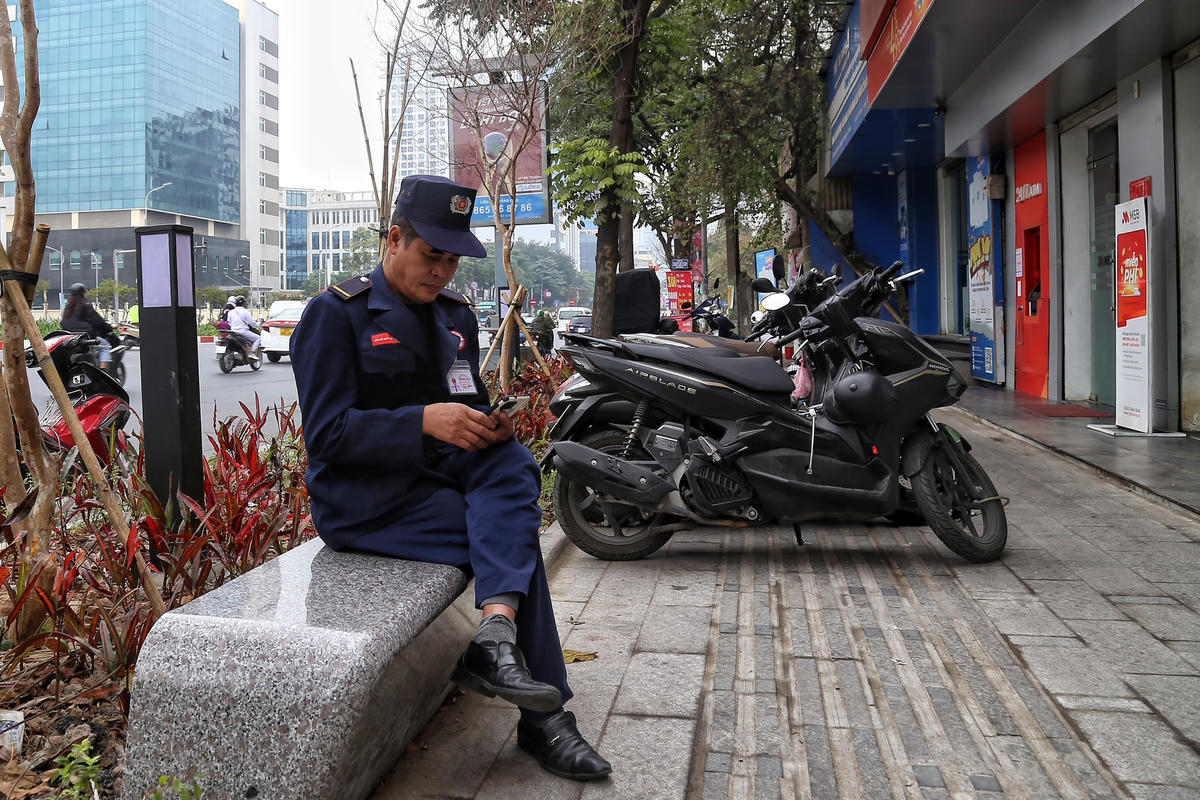 Một bảo vệ thư thả ngồi trông xe trên ghế đá.