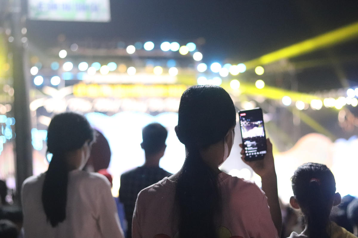 Do đứng quá xa sân khấu nên một số người dân phải bắc ghế lên đứng để theo dõi chương trình. Tại khu vực quảng trường, mọi người tranh thủ sử dụng smartphone để quay lại những khoảnh khắc tại lễ mạc du lịch biển Hải Tiến.