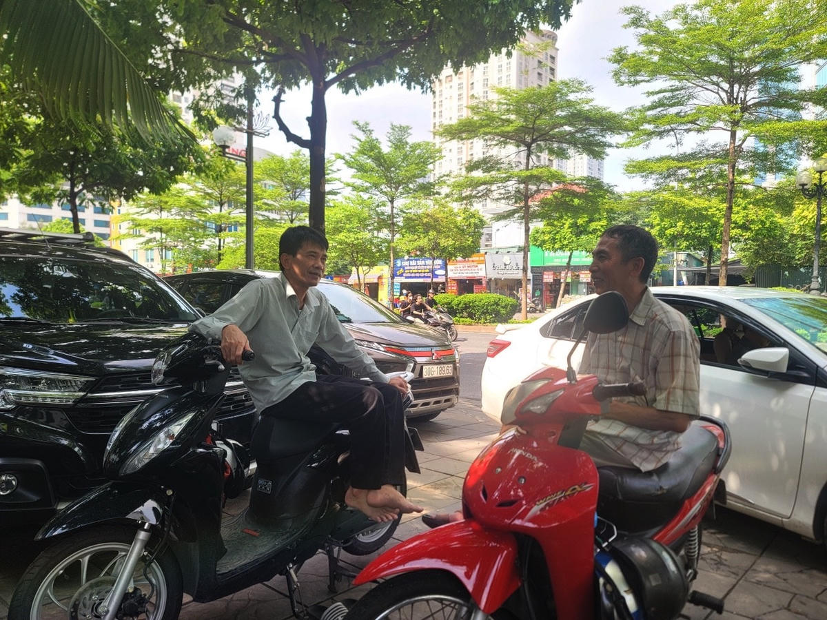 Ông Thanh (53 tuổi, ở Bắc Từ Liêm) đưa con gái đi thi cùng ông Mùi (68 tuổi, ở Long Biên) chở cháu ngoại đi thi ngồi trên xe máy dưới tán cây mát mẻ tỉ tê trò chuyện hỏi han về bài thi môn Ngữ Văn buổi sáng.