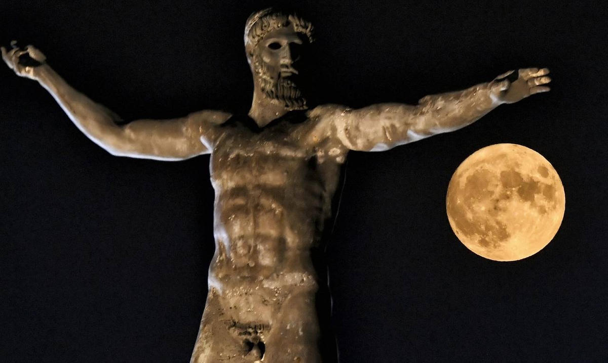 Mặt trăng bên cạnh bức tượng của thần Hy Lạp Poseidon ở thành phố cổ đại Corinth gần ở Athens. Ảnh: AFP.