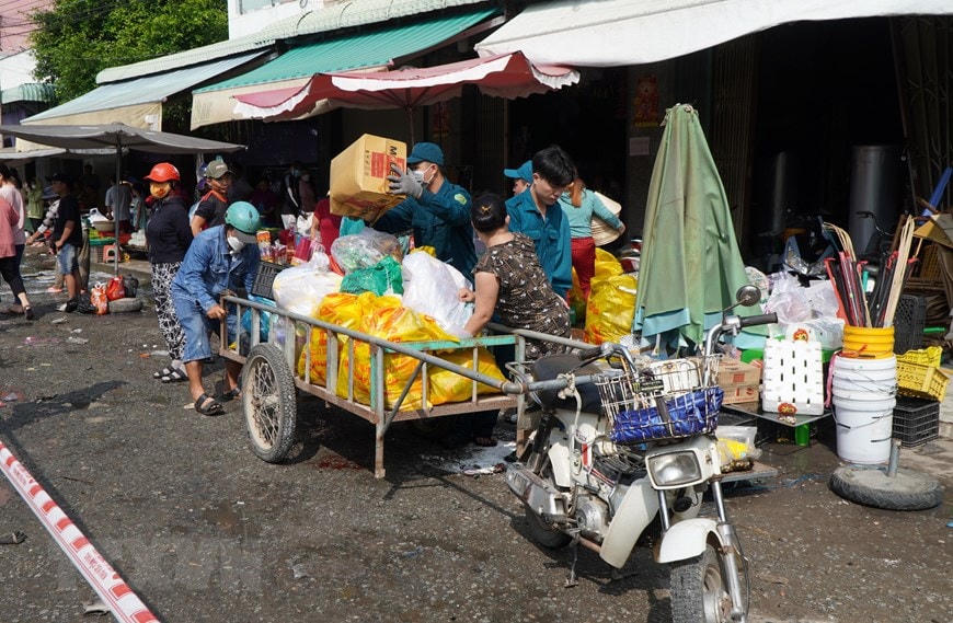 Lực lượng chức năng hỗ trợ người dân mang hàng hóa ra ngoài. Ảnh: Nhựt An/TTXVN.