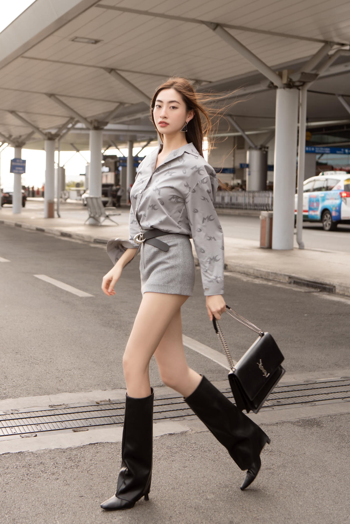 Theo đuổi phong cách gợi cảm, Miss World Vietnam 2019 không mặc các loại váy xẻ như khi đi sự kiện mà mix áo sơ mi cùng chân váy ton-sur-ton metallic mix cùng loạt phụ kiện tông đen như thắt lưng, boots và túi Saint Laurent.
