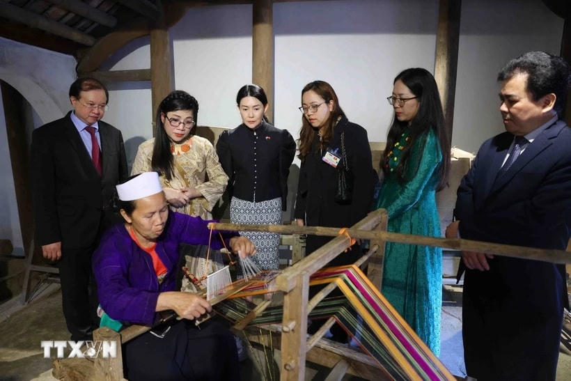 Bà Lê Thị Bích Trân, Phu nhân Thủ tướng Phạm Minh Chính và bà Loo Tze Lui, Phu nhân Thủ tướng Cộng hòa Singapore Lawrence Wong nghe Nghệ nhân giới thiệu về kỹ thuật dệt vải thổ cẩm. (Ảnh: Phạm Kiên/TTXVN)
