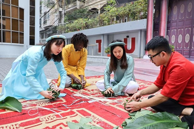 Son và các bạn sinh viên Hàn Quốc chăm chú quan sát người hướng dẫn để thực hành gói bánh chưng.