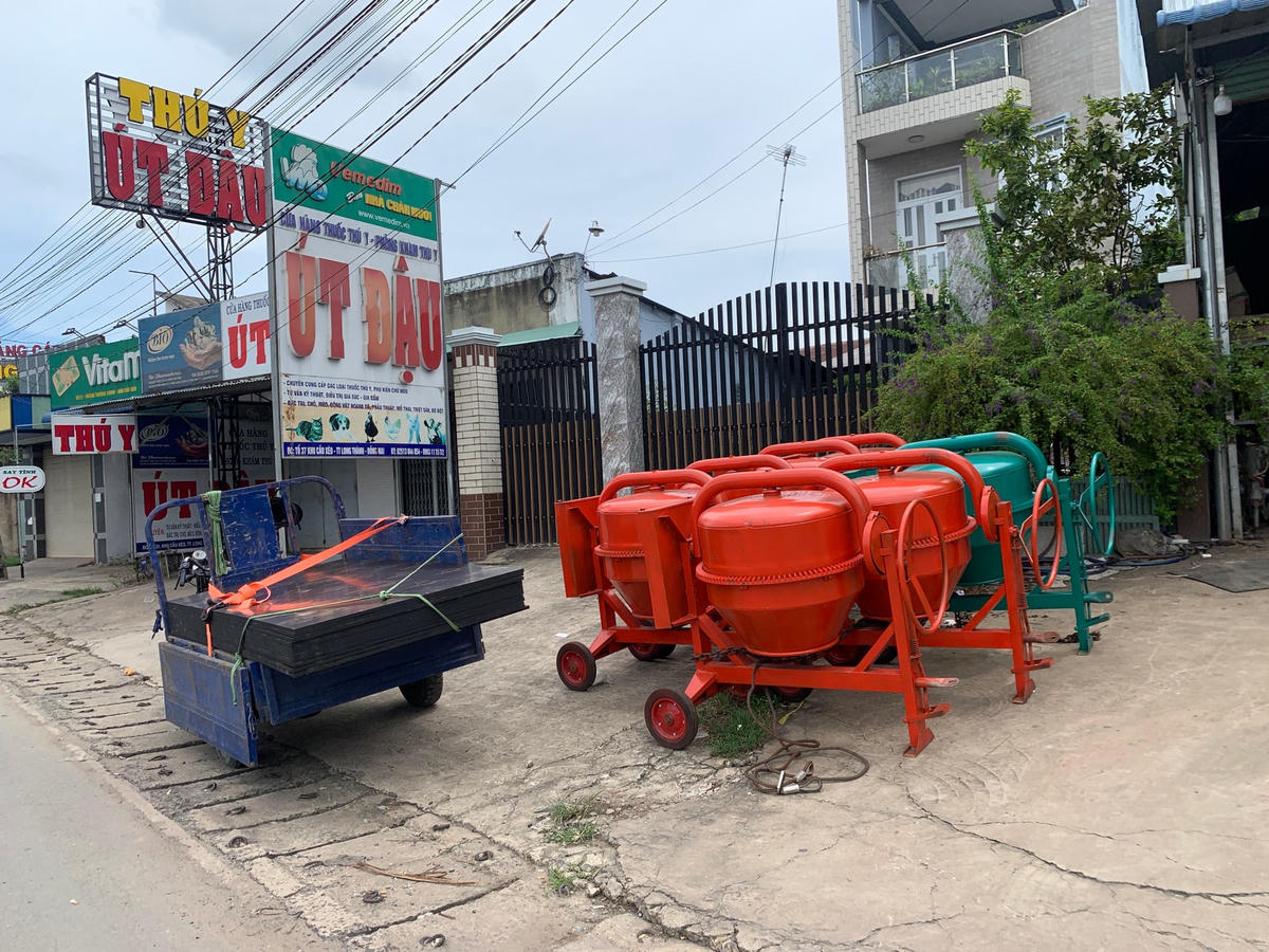 Một chiếc xe 3 bánh đang đợi lên hàng trước một cửa hàng vật liệu xây dựng.
