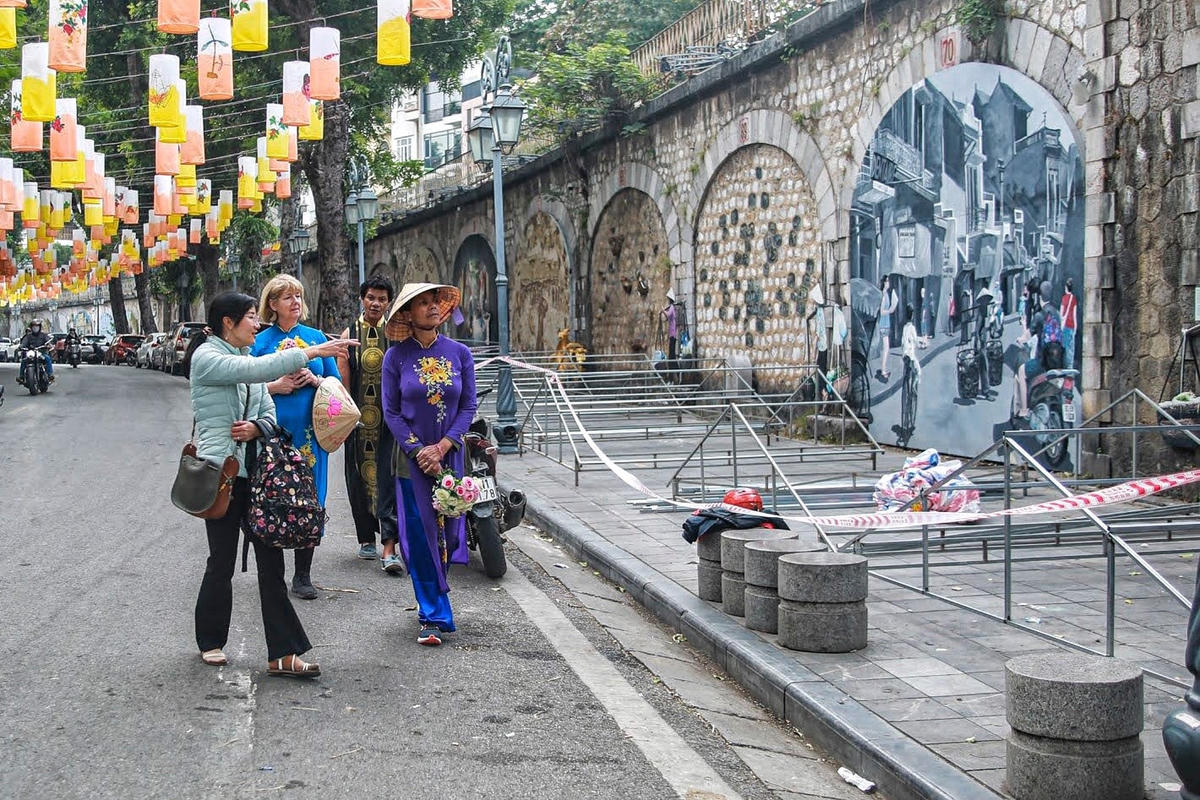 Hướng dẫn viên du lịch đang giải thích ý nghĩa của các bức tranh trên phố bích họa Phùng Hưng.