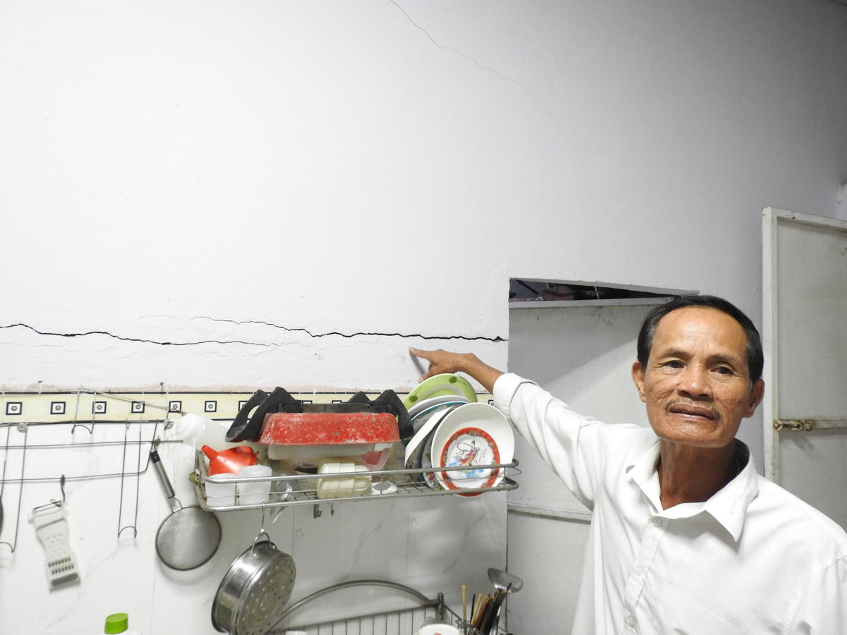 Ông Bùi Chức Quyền, Trưởng Ban công tác Mặt trận Khu dân cư Hòa Phú 2 và bức tường nhà sắp đổ sụp. Ảnh: Thanh Tùng.