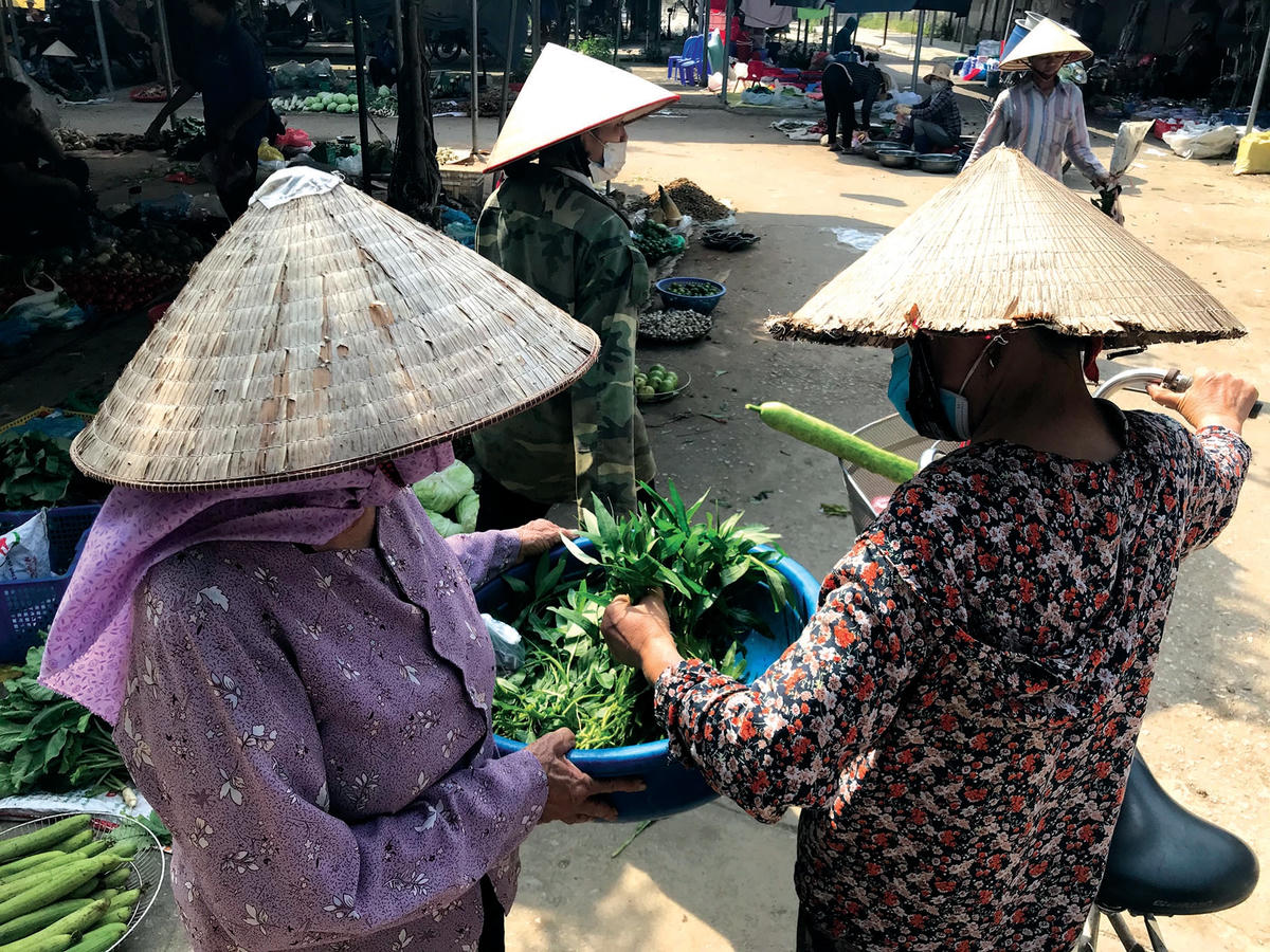 Thay vì ngồi một chỗ, người phụ nữ này có mấy bó rau muống đi dạo quanh chợ để mời người mua nhanh cho hết.  