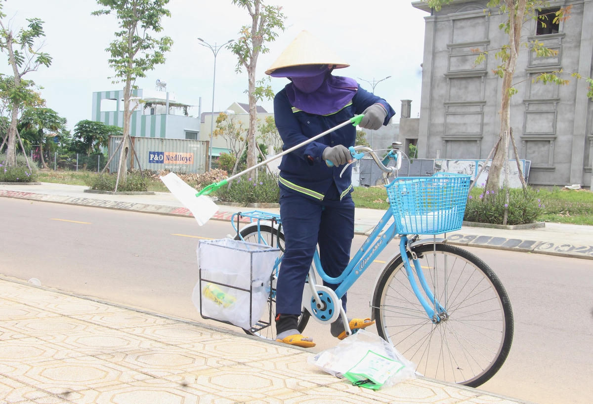 Công nhân đi xe đạp thu gom rác trên vỉa hè.