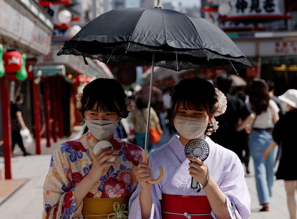 Phụ nữ Nhật Bản mặc kimono mùa hè, sử dụng quạt cầm tay và ô khi đi bộ trên đường phố. Ảnh: Reuters.