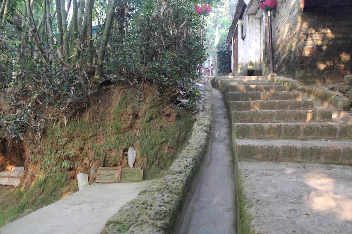 Đường dẫn lên chùa là những bậc đá ong thoai thoải, hai bên là những ngôi nhà cũ và bụi tre xào xạc.  