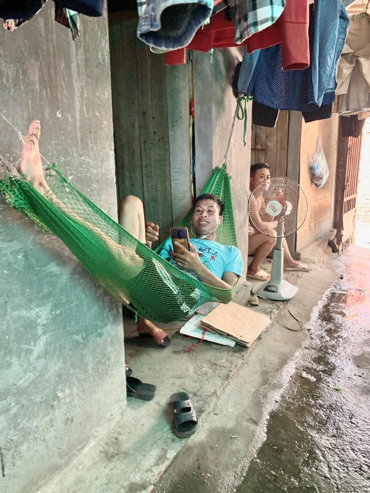 Trong phòng nóng quá, anh Sinh mắc võng trước cửa phòng nằm chơi điện thoại. Ảnh: Hoàng Minh.  