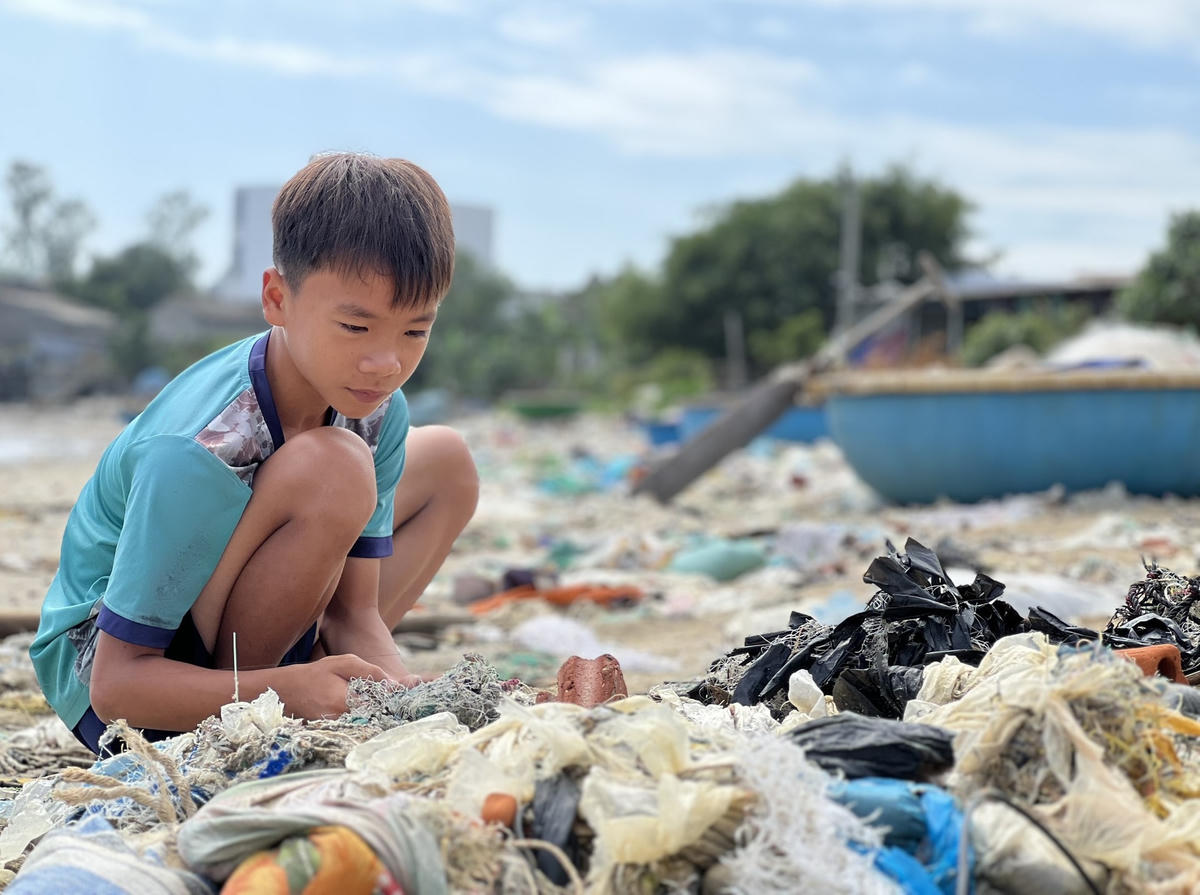 Một em nhỏ vui chơi trên bãi biển tràn ngập rác.