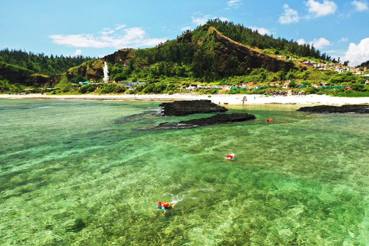 VĐV bơi giữa làng nước biển với rạn san hô đẹp mắt.