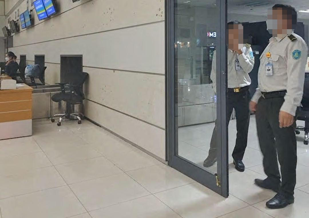 Hai người mặc trang phục an ninh sân bay Cảng hàng không quốc tế Nội Bài hội ý để đưa một hành khách không giấy tờ qua cửa an ninh lên tàu bay sau khi hành khách này chuyển khoản hơn 1 triệu đồng cho đại lý bán vé.. Ảnh: Cắt từ clip.