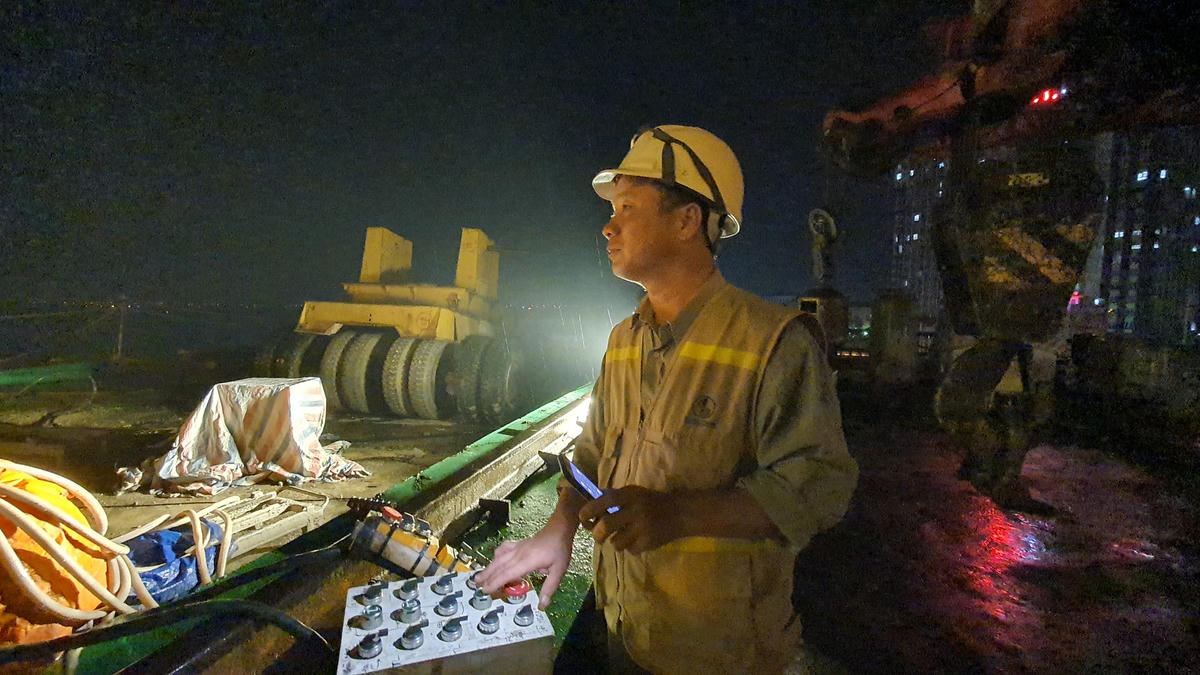 Công nhân điều khiển giá long môn nâng phiến dầm lên xe siêu trường siêu trọng.