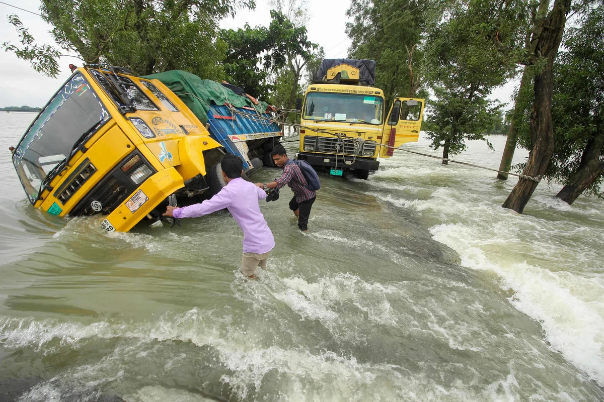 Những người đàn ông vật lộn trong nước lũ bên cạnh một chiếc xe tải bị lật trên một con đường ở Sunamganj.