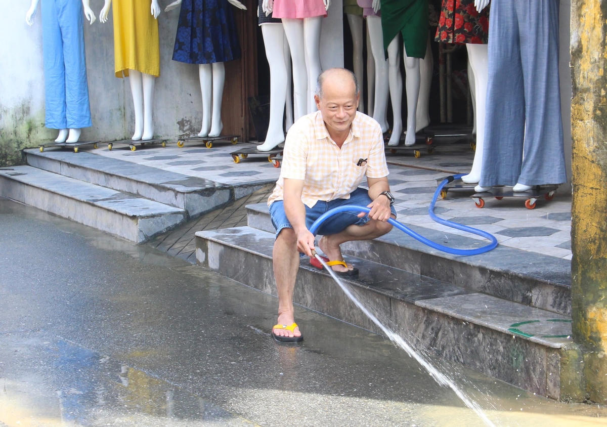 Ông Trần Vĩ Chí dùng vòi nước xịt rửa trôi lớp bùn non.