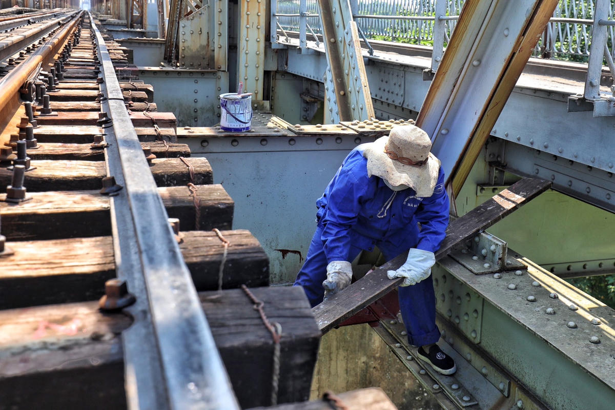 Để có thể có chỗ đứng, ngồi dưới gầm đường sắt và để hộp sơn, công nhân phải đưa các thanh gỗ gá lên các thanh thép.