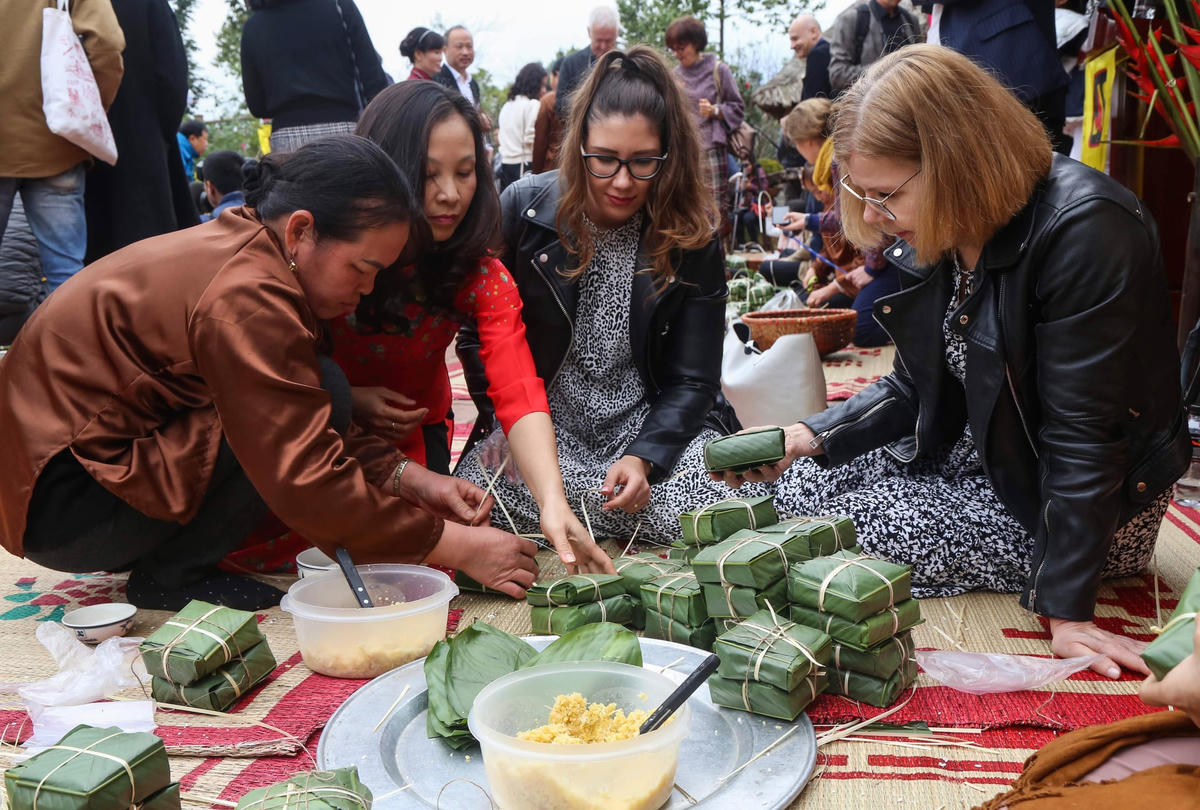 Du khách quốc tế trải nghiệm gói bánh chưng. Ảnh: Quang Vinh.