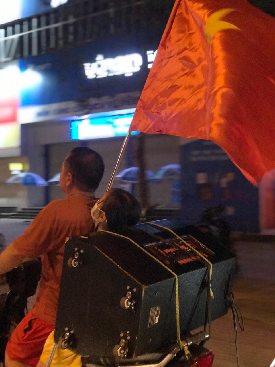Người bố đánh xe máy chở theo con gái, không quên kẹp thêm loa thùng và cờ đỏ sao vàng.