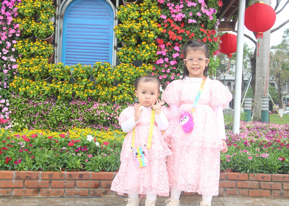 Các em nhỏ tạo dáng bên tiểu cảnh hoa.