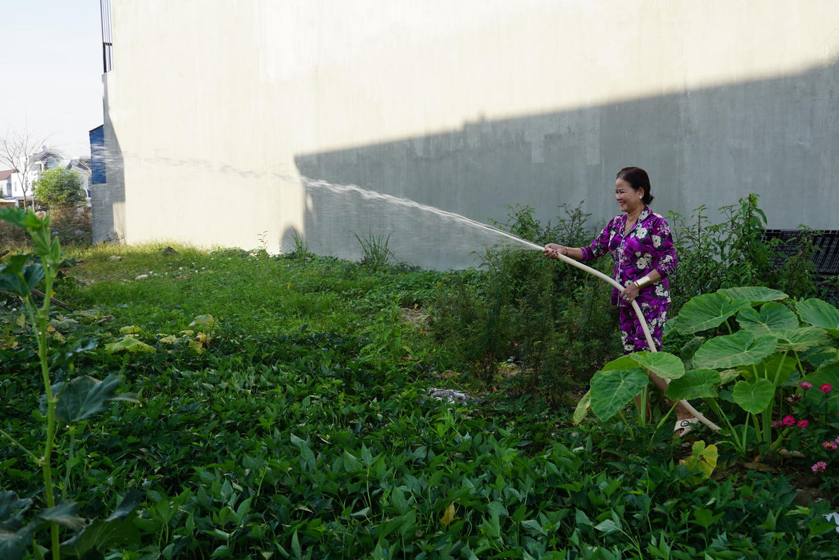 Bà Nguyễn Luận - cư dân tại khu TĐC cười tươi bên vườn rau trồng ở khu đất trống chủ đất chưa xây dựng. Ảnh: Mạnh Thìn.