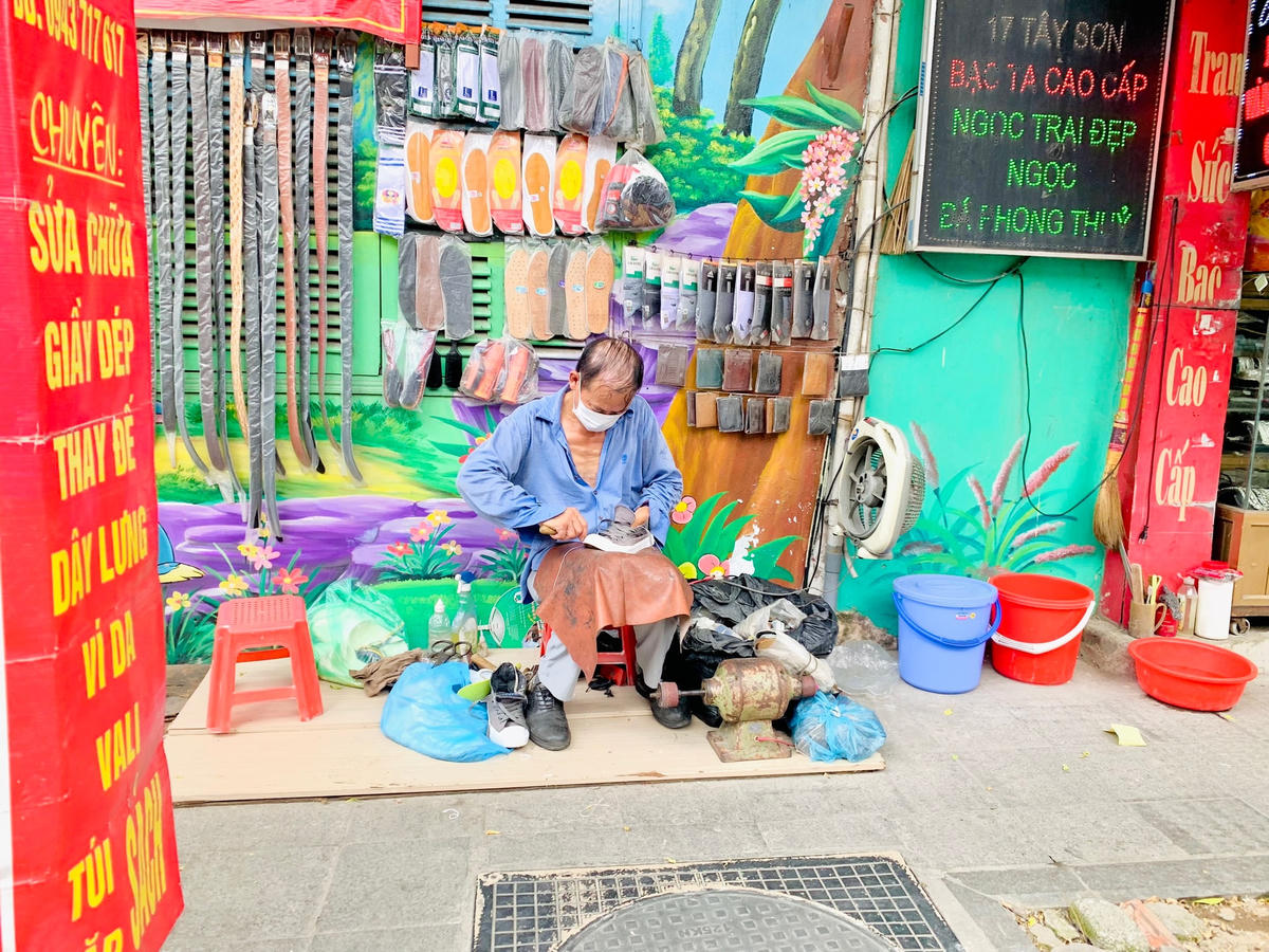 Một người làm nghề sửa giày dép ngoài vỉa hè chật vật mưu sinh dưới thời tiết nắng nóng.