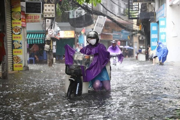 Sáng nay, nhiều người dân phải dắt bộ xe máy vì không thể di chuyển trong tình trạng ngập úng nặng. Ảnh: TTXVN.