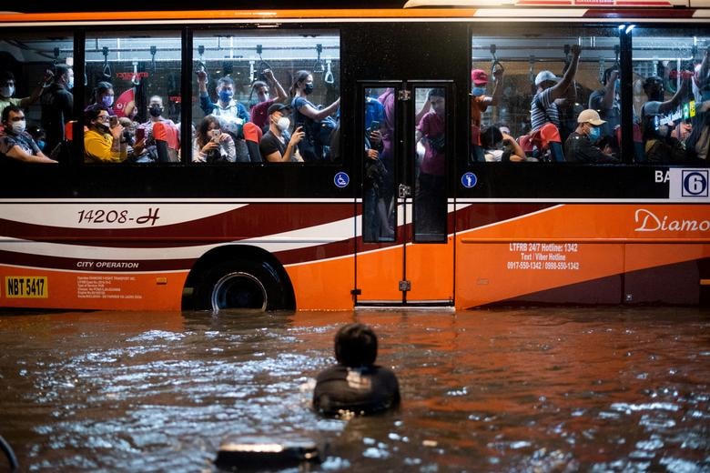 Một đứa trẻ bơi trong nước lũ do mưa lớn khi một chiếc xe buýt chở khách đi ngang qua, ở Manila, Philippines.