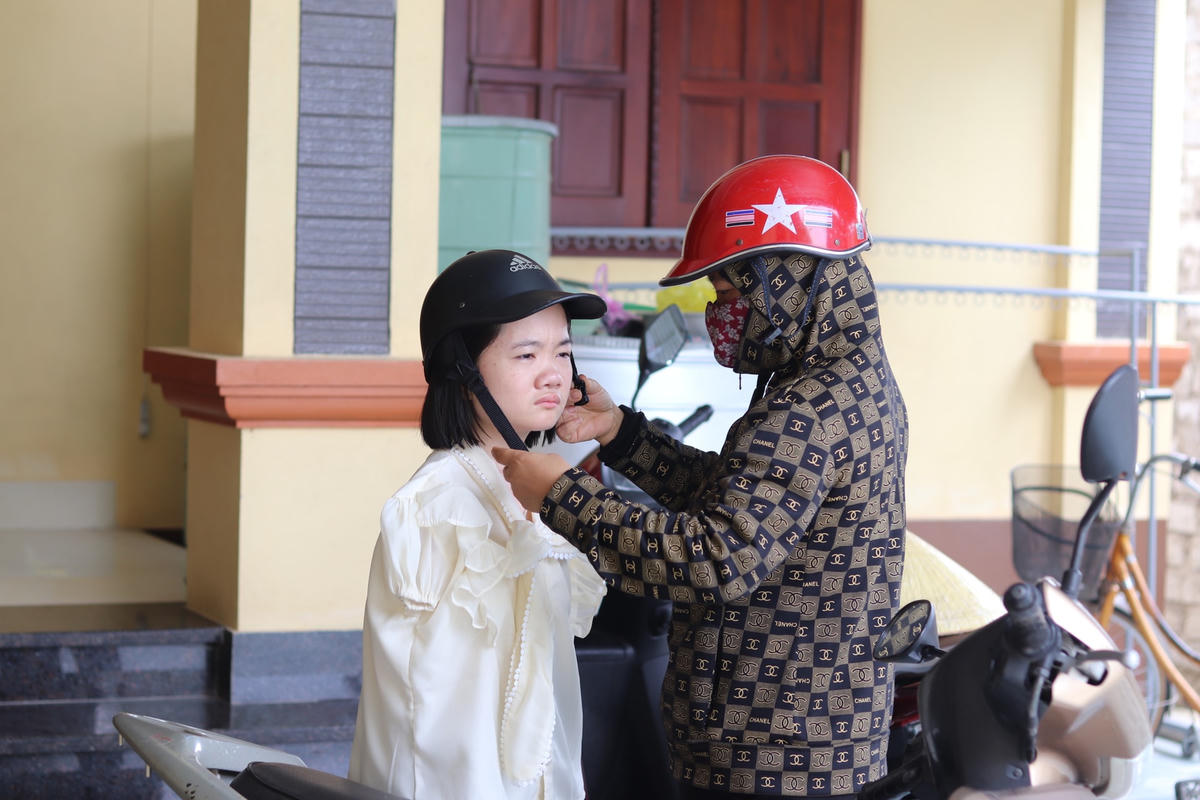 Cô Nguyễn Thị Tình nhẹ nhàng cài quai mũ bảo hiểm cho con gái. Ảnh: Đình Minh