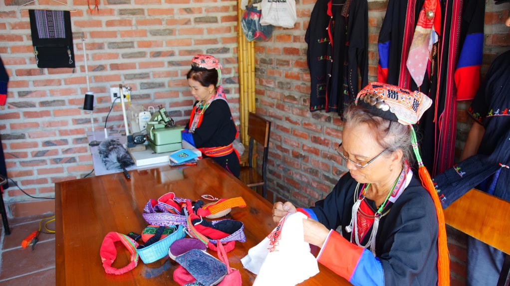 Phụ nữ Dao Thanh Y trình diễn nghệ thuật thêu truyền thống và bán các sản phẩm thủ công từ nghề thêu cho du khách tại Mô hình du lịch cộng đồng xóm Gốc Đa, thôn Khe Sú 2.