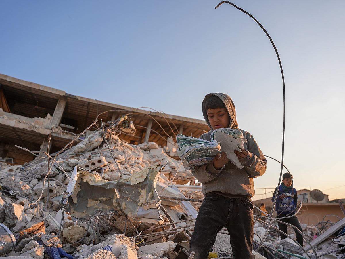 Cậu bé đọc quyển sách nhặt được từ đống đổ nát ở thành phố Jenderes (Syria). ẢNH: AFP.  