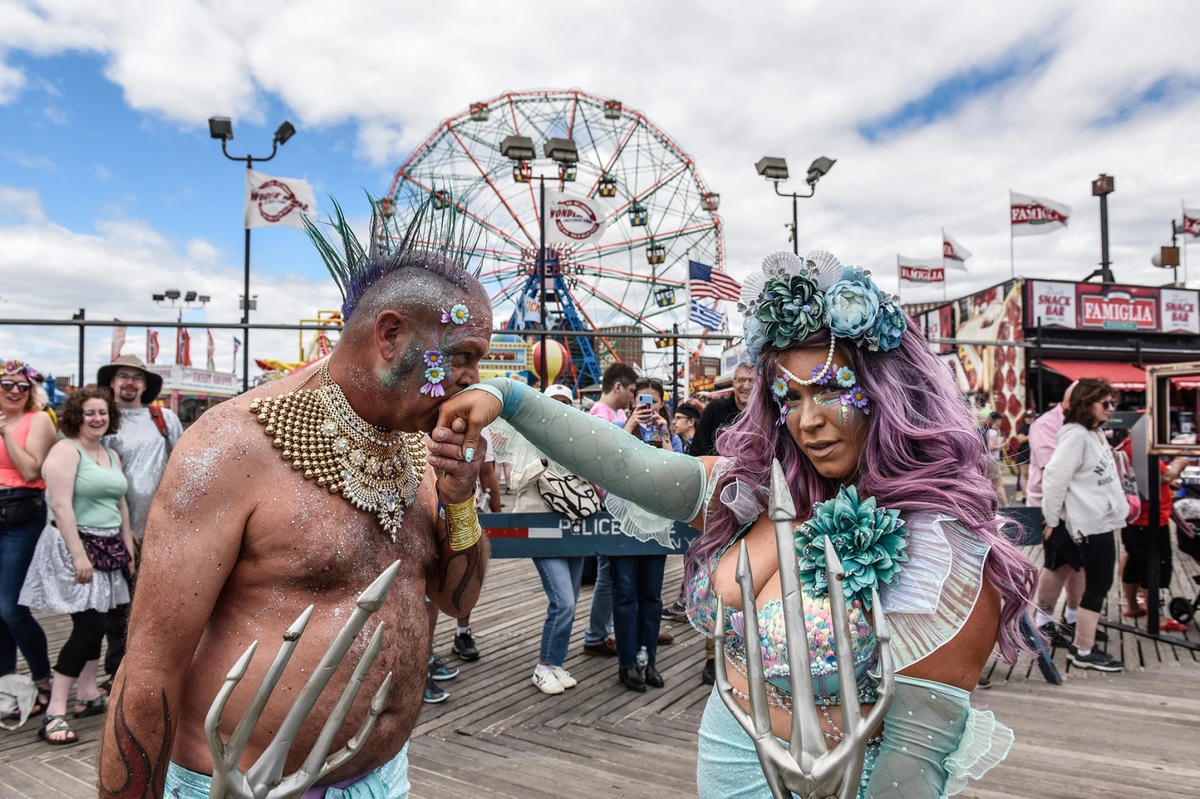 Một người đàn ông hôn tay con gái của mình trên lối đi bộ lót ván Coney Island.