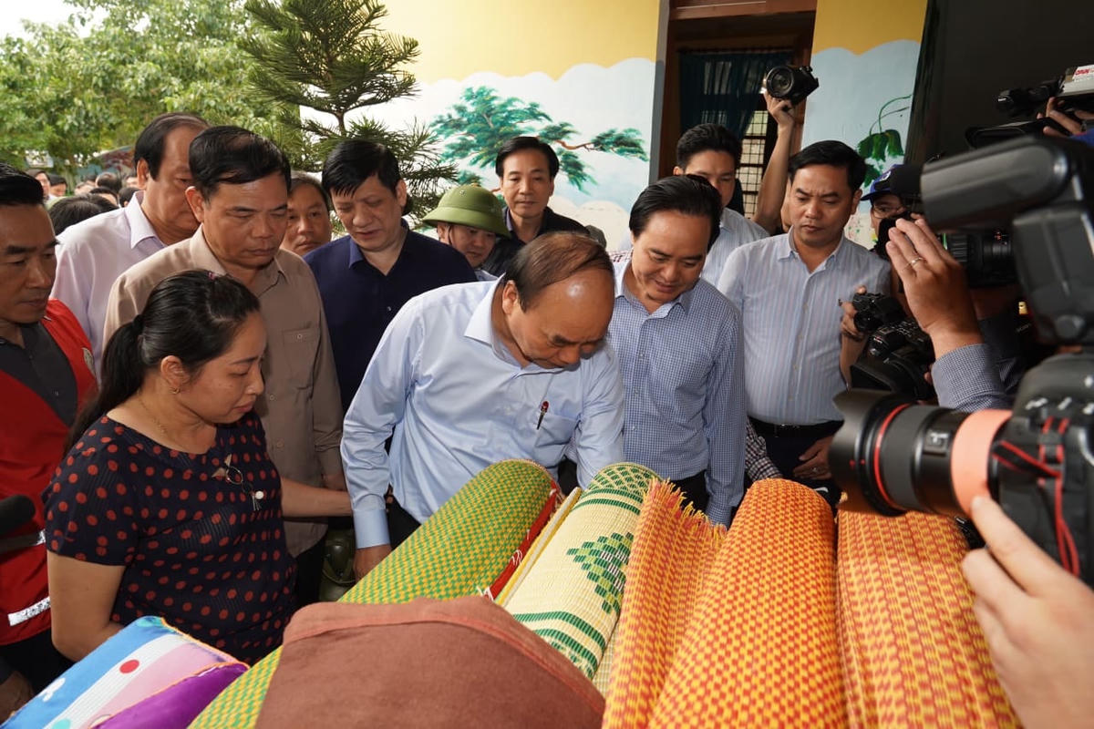 Thủ tướng Nguyễn Xuân Phúc xem sản phẩm hàng hóa của bà con bị ngấm nước. Ảnh: Quang Hiếu.
