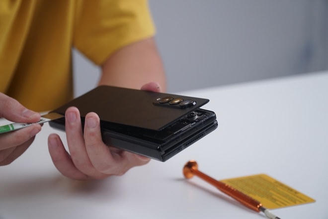 Để tiếp cận các linh kiện bên trong, kỹ thuật viên cần tháo mặt lưng của máy bằng cách khò nhiệt hoặc hấp nóng để làm tan chảy phần keo.