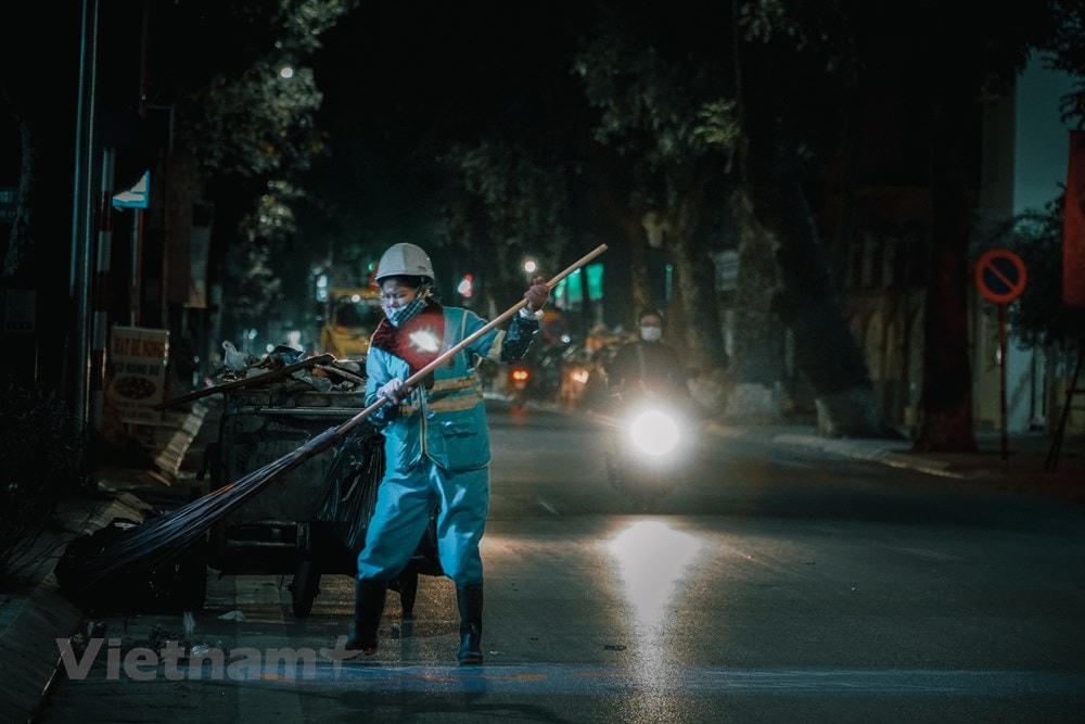 Chị Nguyễn Thị T., 42 tuổi đang bắt đầu công việc thường ngày của mình là dọn dẹp vệ sinh đường phố tại con phố Lò Đúc, chỉ có điều hôm nay trời rét hơn. Chị chia sẻ: “Nghề của tôi nhìn chung là vất vả. Thu rác xong chúng tôi phải đợi xe tải đến lấy rác mới được nghỉ. Hôm nào may mắn xe đến sớm tầm 1 hay 2h sáng thì được nghỉ sớm, không thì phải trắng đêm.” (Ảnh: Minh Hiếu/Vietnam+).