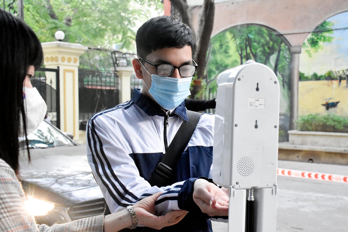 Học sinh Trường THPT Việt Đức được cô giáo hướng dẫn đo thân nhiệt, sát khuẩn tay. 