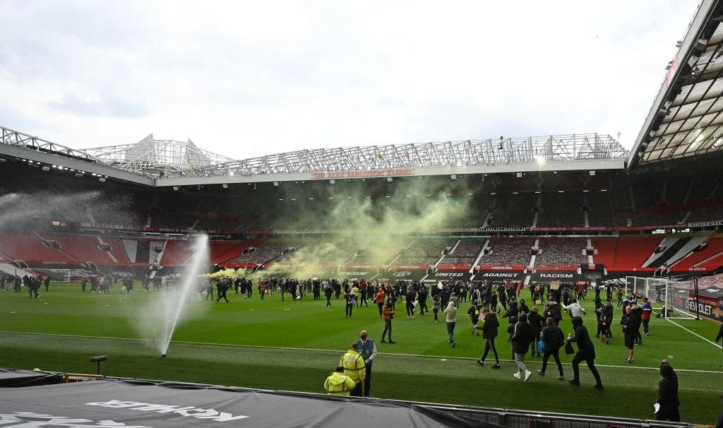 Người hâm mộ đi trên mặt sân cỏ tại Old Trafford. Nhiều cổ động viên vào sân khiến việc đảm bảo an ninh cho trận đấu bị xâm phạm.