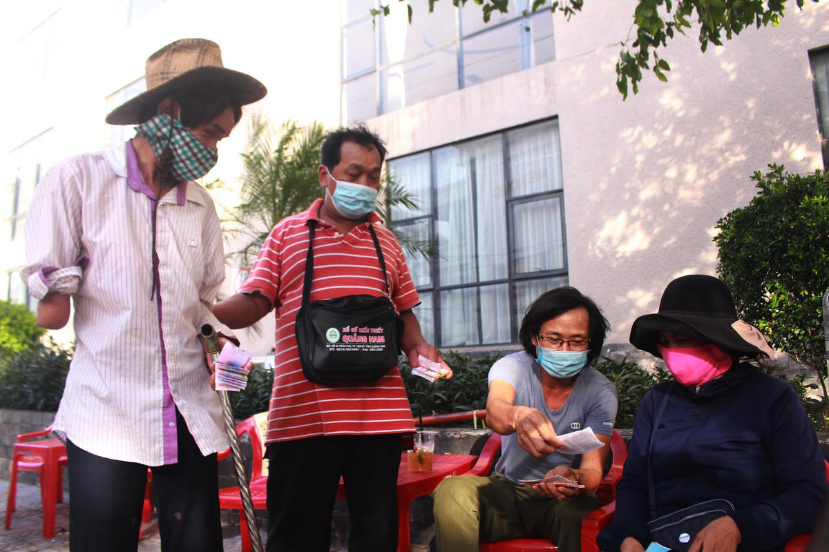 Ông Lê Quang Quỳnh (ngoài cùng bên trái) được một người bạn dắt đi bán vé số dạo ở TP Đông Hà, Quảng Trị.