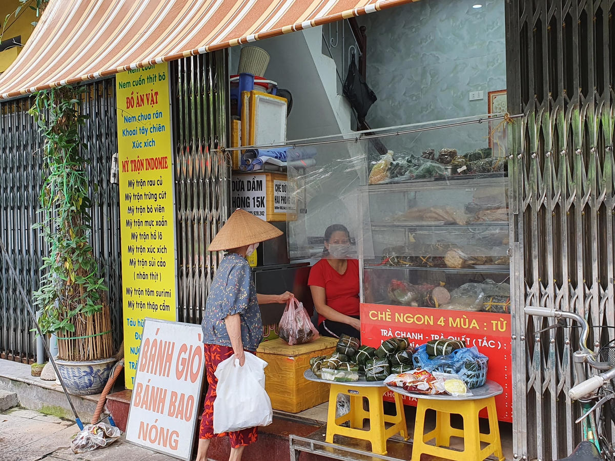Bà Phạm Thị Tuyến (72 tuổi) đang mua bánh giò tại một quán nhỏ nằm trên đường Lê Hồng Phong. Cửa hàng có đặt tấm chắn chống giọt bắn để đảm bảo an toàn và giãn cách.