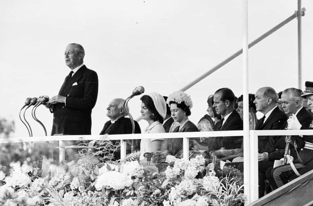 Harold Macmillan đọc diễn văn tại đài tưởng niệm John F Kennedy. Đứng sau ông trên khán đài là Jackie Kennedy, Nữ hoàng Elizabeth II, Hoàng thân Philip và Thủ tướng Anh Harold Wilson, năm 1965.