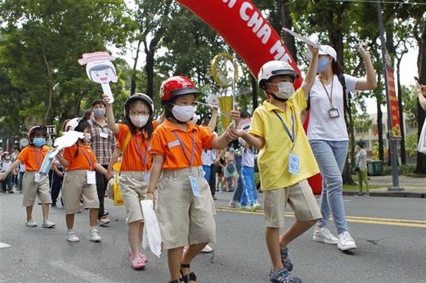 Các em học sinh tiểu học cùng phụ huynh và thầy cô giáo đi bộ vận động toàn dân 'Đội mũ bảo hiểm cho trẻ em' trên đường Lê Duẩn, quận 1, Thành phố Hồ Chí Minh. (Ảnh: Thanh Vũ/TTXVN).