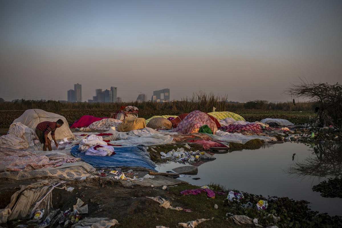 Một "dhobi", hay người giặt giũ, giặt đồ trên vùng ngập lũ sông Yamuna ở New Delhi. Dhobis là những công nhân giặt là truyền thống, giặt quần áo bằng tay và phơi dưới ánh nắng mặt trời, một nghề đã tồn tại qua nhiều thế hệ. Nghề truyền thống này vẫn phổ biến ở Ấn Độ bất chấp những công nghệ hiện đại. Ảnh: Altaf Qadri / AP.