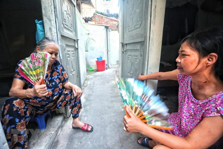 Nhiều bệnh nhân ở xóm chạy thận Lê Thanh Nghị chọn cách ra cửa ngồi quạt tay để chống chọi với cái nóng như thiêu đốt trong những căn phòng trọ chật hẹp. (Ảnh: Thành Đạt/TTXVN).