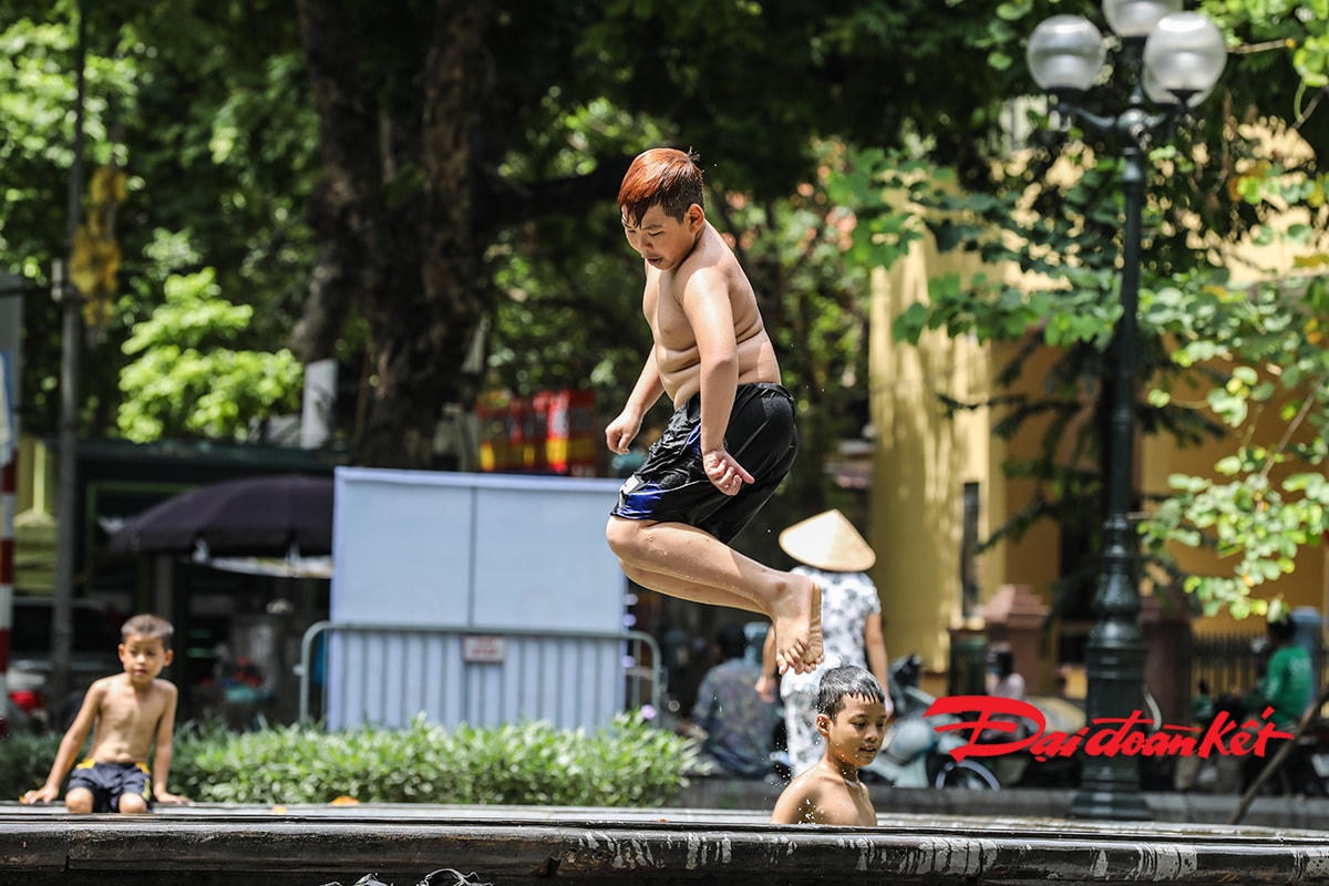 Trẻ em vô tư tắm tại vòi phun nước ở nơi công cộng đông người.